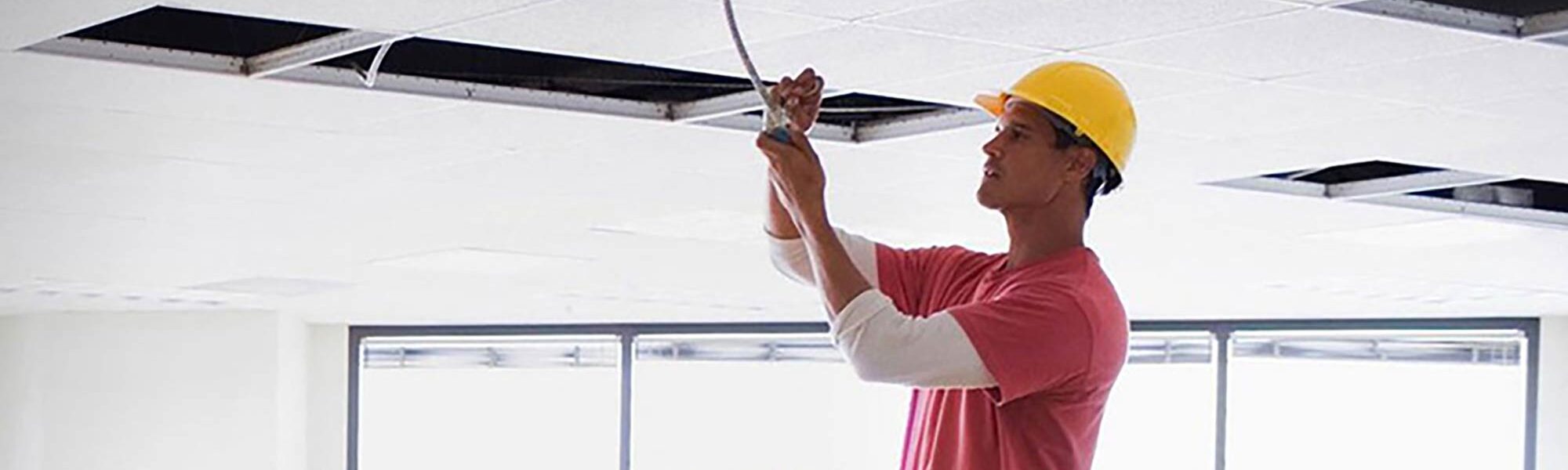 A contractor installing light fixtures in a drop ceiling